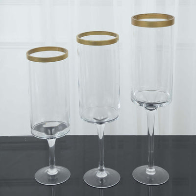 Set of three elegant glass vases with gold rims on a black surface.