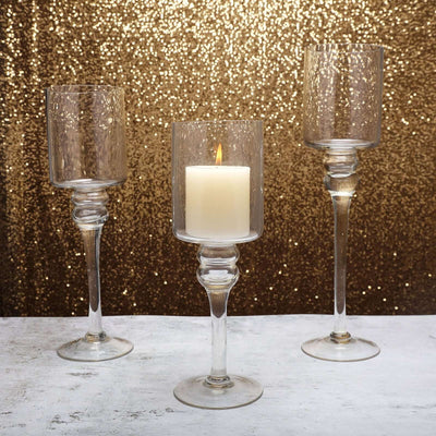 Elegant glass candle holders with a lit candle on a sparkly gold backdrop.