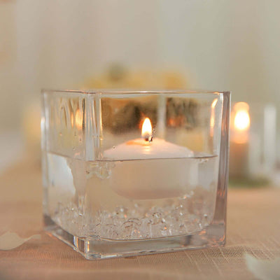 Floating candle in a glass holder filled with water and decorative stones.