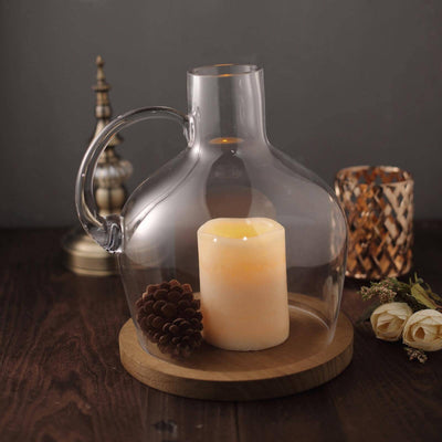 Glass candle holder with pinecone on wooden base, lit candle inside.