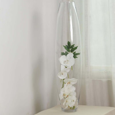 Tall glass vase with white orchids and green leaves.