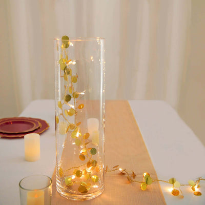 Glass vase with decorative fairy lights and greenery for table decor.