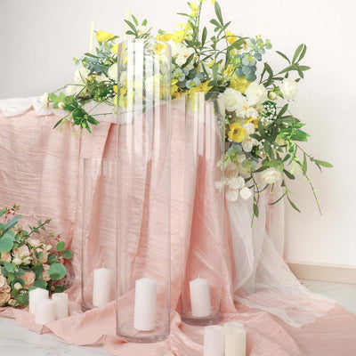 Elegant glass vases surrounded by fresh flowers and candles on a soft pink tablecloth.