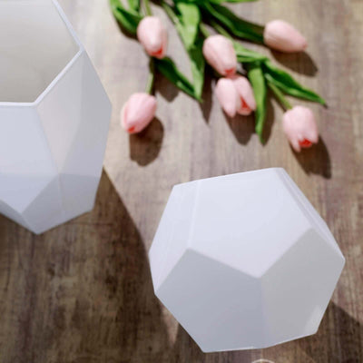 Geometric white vases with pink tulips on a wooden surface.