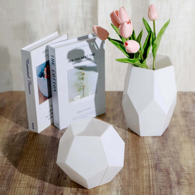 Geometric white vases with pink tulips and books on a wooden surface.