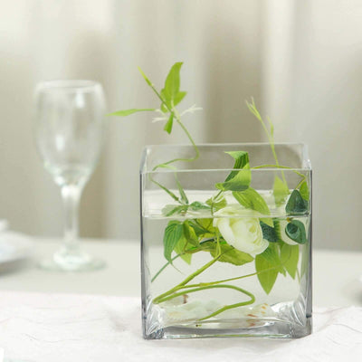 Clear glass vase with white roses and greenery in water.