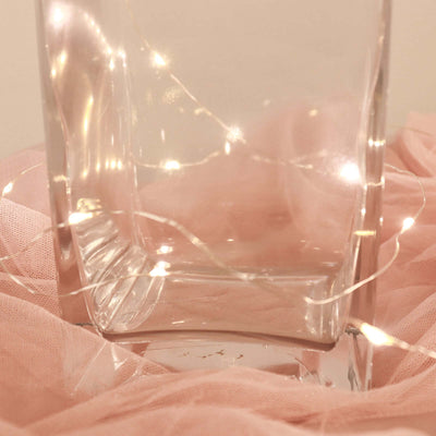Clear glass vase with warm fairy lights, elegantly styled with soft pink fabric.
