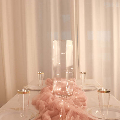 Elegant table setting with a transparent centerpiece and soft pink drapery.