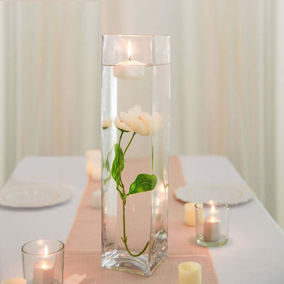Elegant glass vase with floating candles and white flowers on a table.