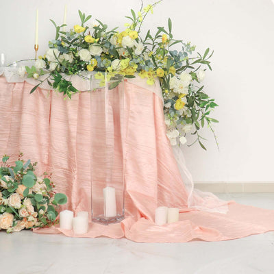Floral arrangement and candles on a draped table in soft pastel tones.