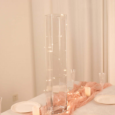 Glass vase with string lights on a dining table setting.
