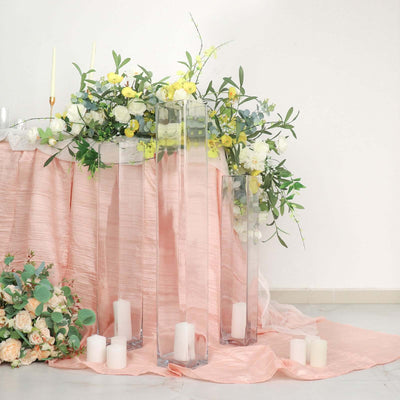 Elegant floral arrangement with glass vases and candles on a pink tablecloth.