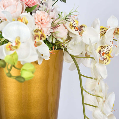 Gold vase with white orchids and pink flowers on a plain background.