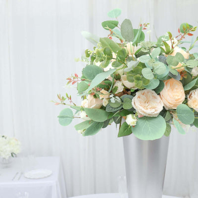 Elegant floral arrangement in a silver vase with soft peach and green hues.