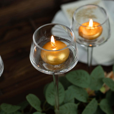 Glass candle holder with a golden candle flame surrounded by greenery.