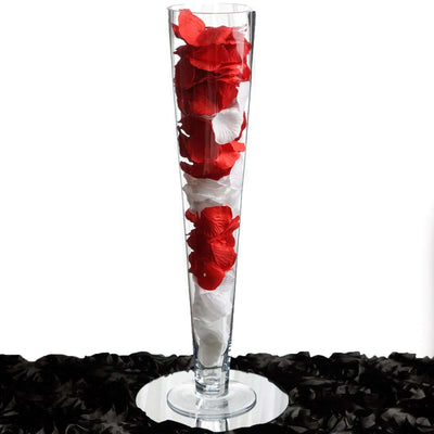 Clear vase filled with red and white rose petals on a mirrored surface.