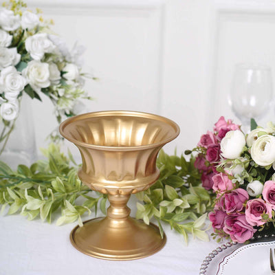 Gold decorative pedestal vase with floral arrangements around it.