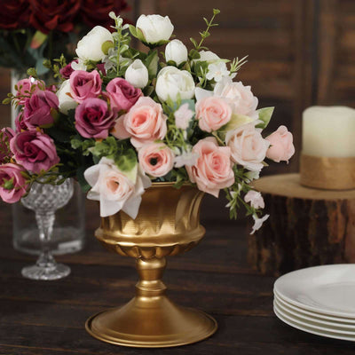 Gold vase with mixed roses and tulips arrangement on a wooden table.