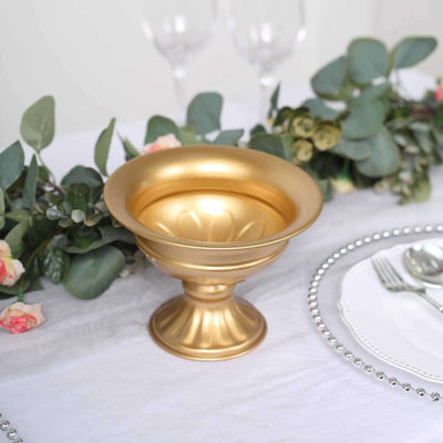 Gold decorative bowl on a table with greenery and flowers.