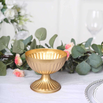 Gold decorative bowl with fluted design on a table with floral arrangements.