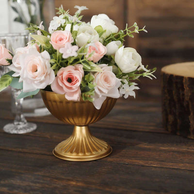 Gold vase filled with pink and white flowers on a wooden table.