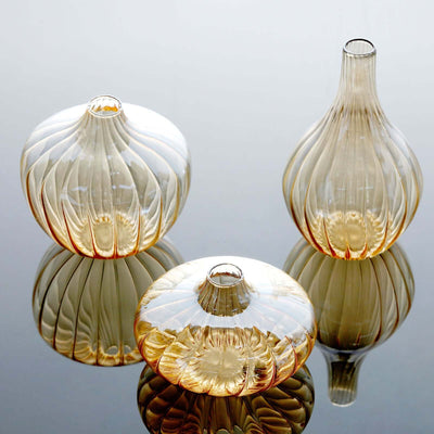Three elegant glass vases in amber hues reflecting on a smooth surface.