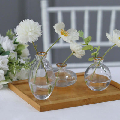 Three glass vases with flowers on a wooden tray.