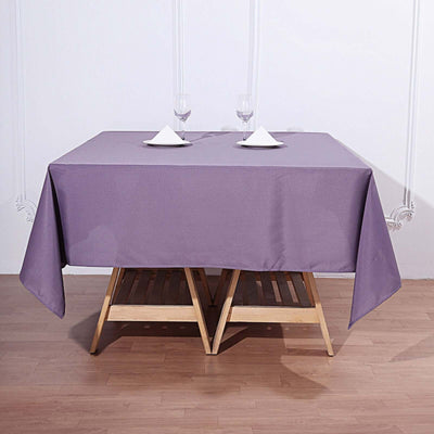Purple tablecloth draped over a wooden table with glasses and napkins.