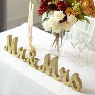 Gold "Mr & Mrs" sign with flowers and candles on a table.