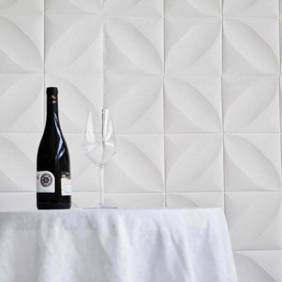 Wine bottle and glasses on a table against a textured white wall.