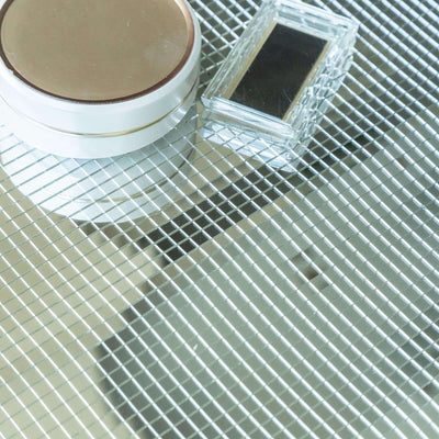 Cosmetic products on a reflective surface, including a compact and a small container.