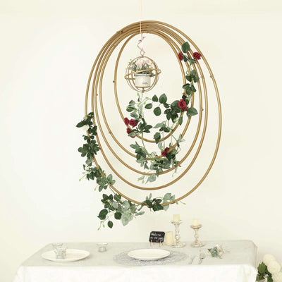 Hanging gold circular frame with greenery and flowers above a dining table
