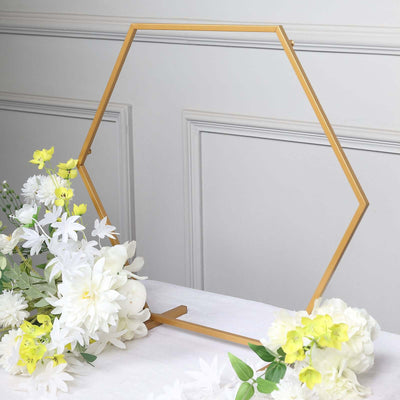 Gold hexagon frame with white and yellow flowers on a table.