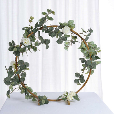Gold circular floral arrangement with greenery and white roses on a plain backdrop.