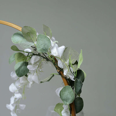 Artificial white floral arrangement with green leaves on a gold hoop.