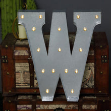 A large silver metal letter W sits on top of a wooden trunk