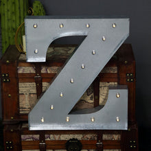 A vintage silver metal letter Z sits on top of a wooden trunk, indoor lighting