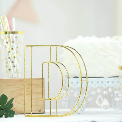 Gold wire letter "D" decor on a table with cake and party supplies.