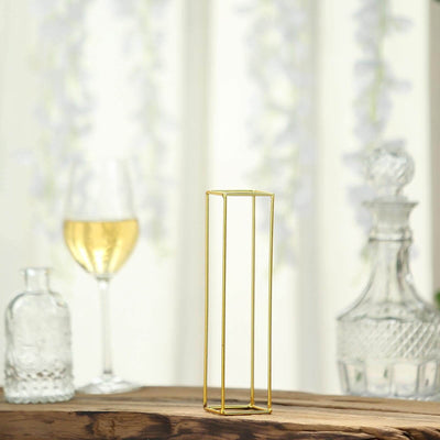 Gold metal vase on a wooden table with decorative glassware in the background.