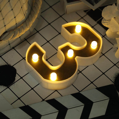 Illuminated number 3 candle on a patterned surface.