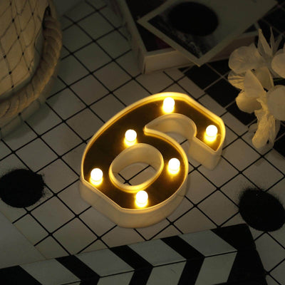Number 6 decorative light with warm yellow bulbs on a patterned surface.