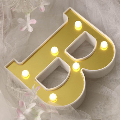 Decorative illuminated letter 'B' in gold and white with soft lighting.