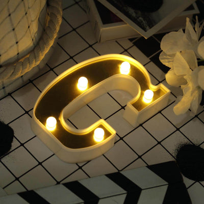 Decorative letter C light with warm glow on patterned surface.