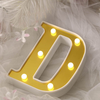 Decorative illuminated letter "D" with yellow lights on a soft fabric background.