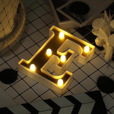 Illuminated letter "E" decorative sign with lights on a patterned surface.