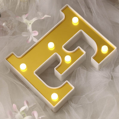 Yellow illuminated letter "E" decorative sign on soft fabric background.