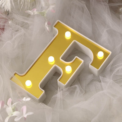 Gold letter F marquee light on soft white fabric backdrop.