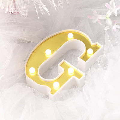 Light-up letter "G" sign with yellow accents on a soft white background.