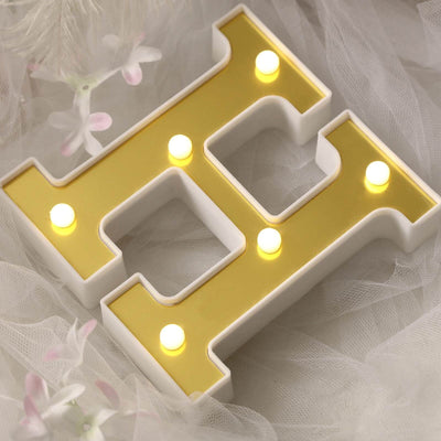 Decorative illuminated letter "H" sign with gold and white design.