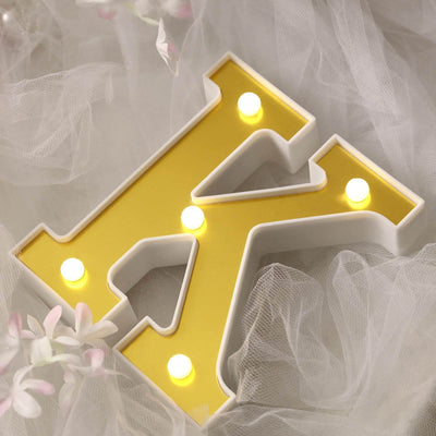 Yellow light-up letter "K" on soft white fabric backdrop.